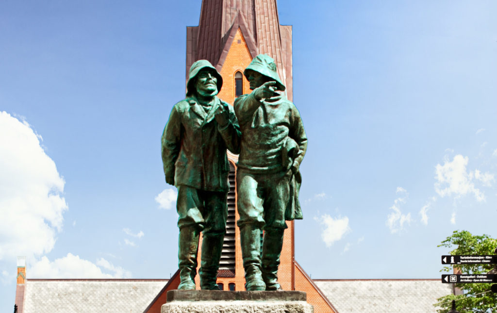 Skulptur av to fiskere foran en murbygning